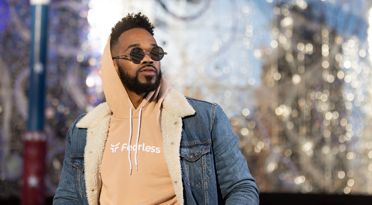 Model standing in tan fearless hoodie with sunglasses on. 