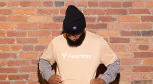 Model standing against brick wall with tan fearless t-shirt and black fearless beanie